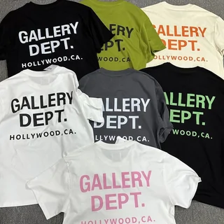 Six short-sleeve printed T-shirts in black, olive, cream, white and grey, spread out on a dark floor